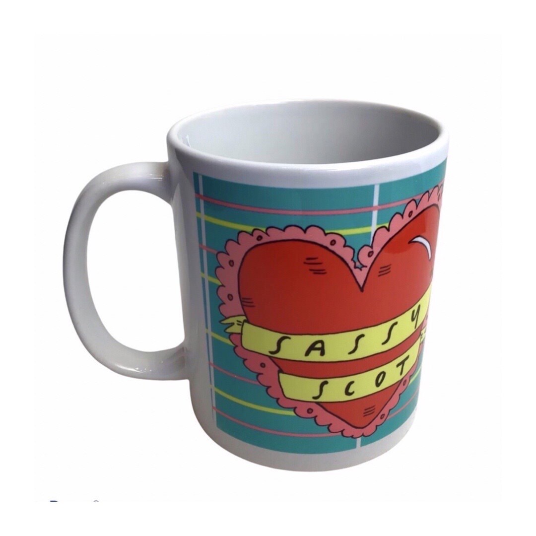 This mug features an illustration of a large red love heart on a blue tartan background and the text 'Sassy Scot' written inside a yellow banner.