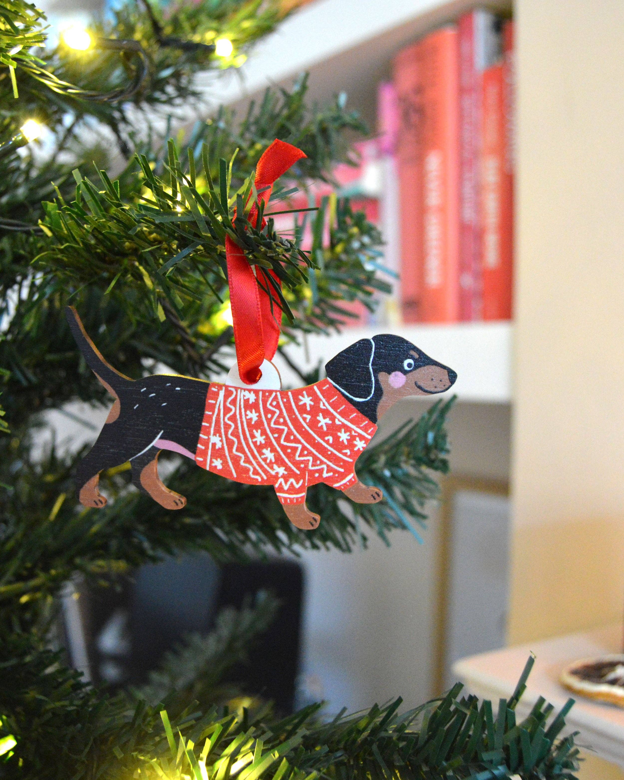 Decorative Christmas ornament of a dachshund in a sweater on a lit Christmas tree.