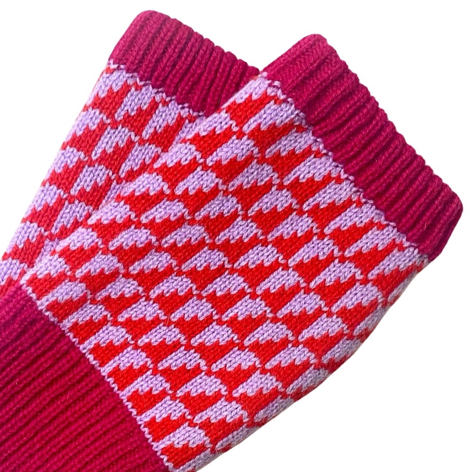 A close-up of a pair of knit wrist warmers in red and pink, featuring a repeating houndstooth pattern and ribbed cuffs.