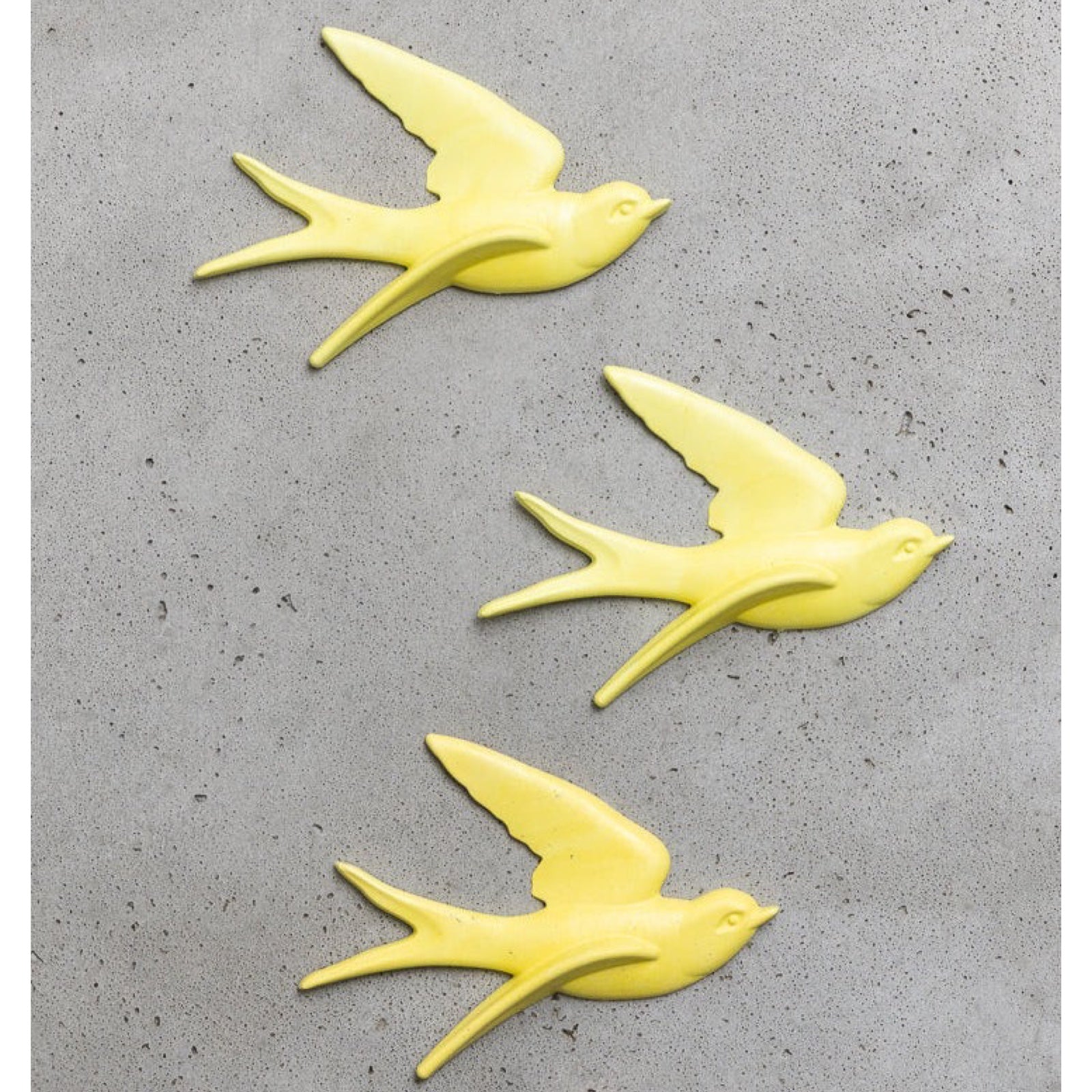 Three yellow bird-shaped wall decorations on a grey surface.