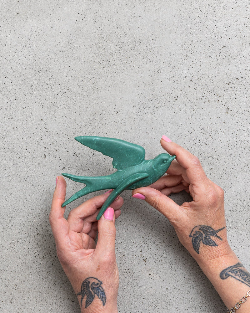 Person holding a green ceramic swallow figurine against a gray background.