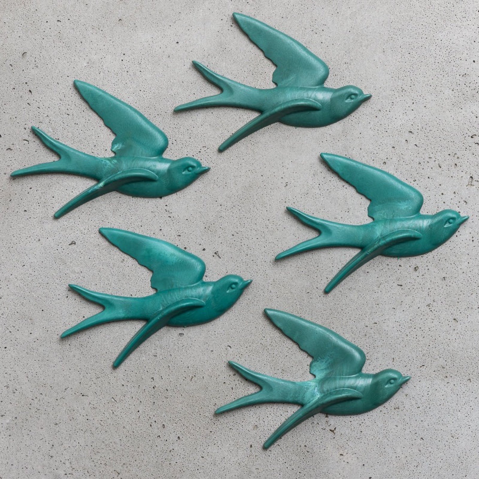 Five turquoise bird-shaped wall decorations on a concrete surface.