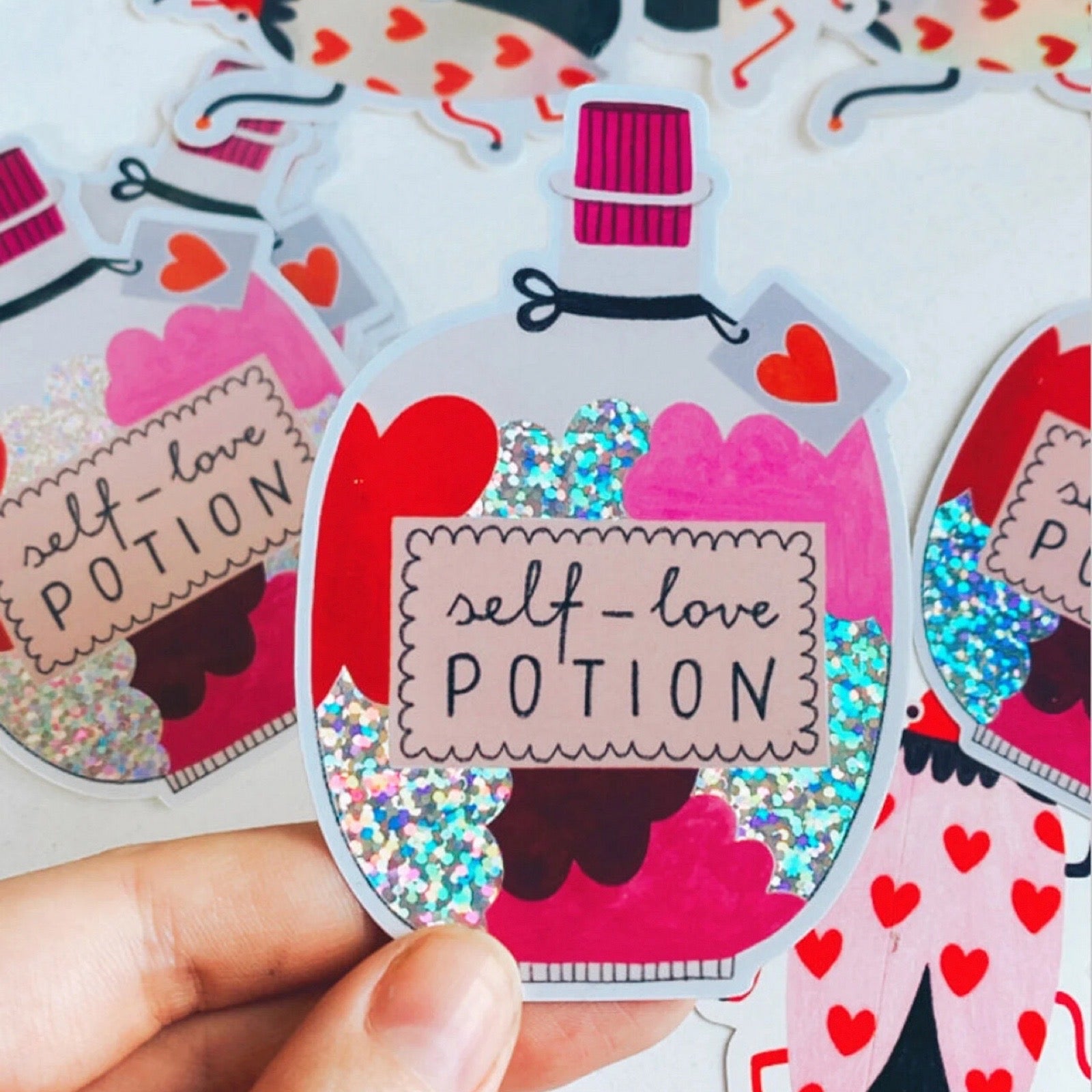 Sticker of a potion bottle labeled 'self-love potion' held by a hand.