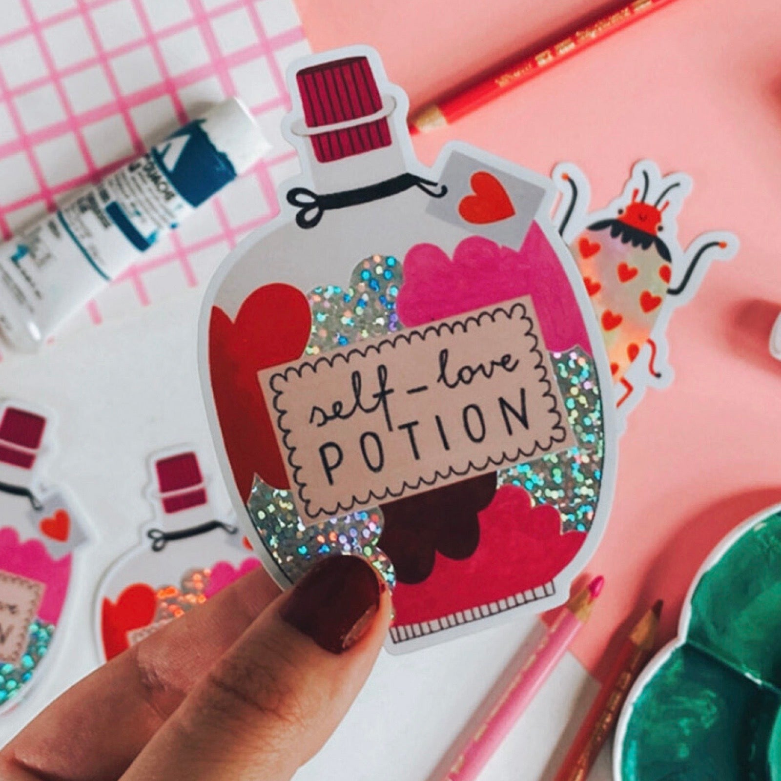 Sticker of a potion bottle labeled 'self-love potion' held by a hand with a colourful background.