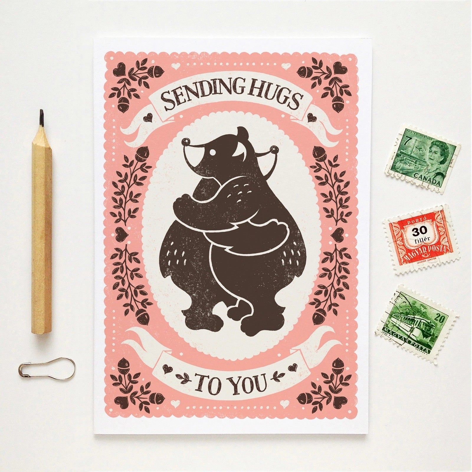 Card with bear illustration and text 'Sending Hugs To You' on a white background with stamps and a pencil.