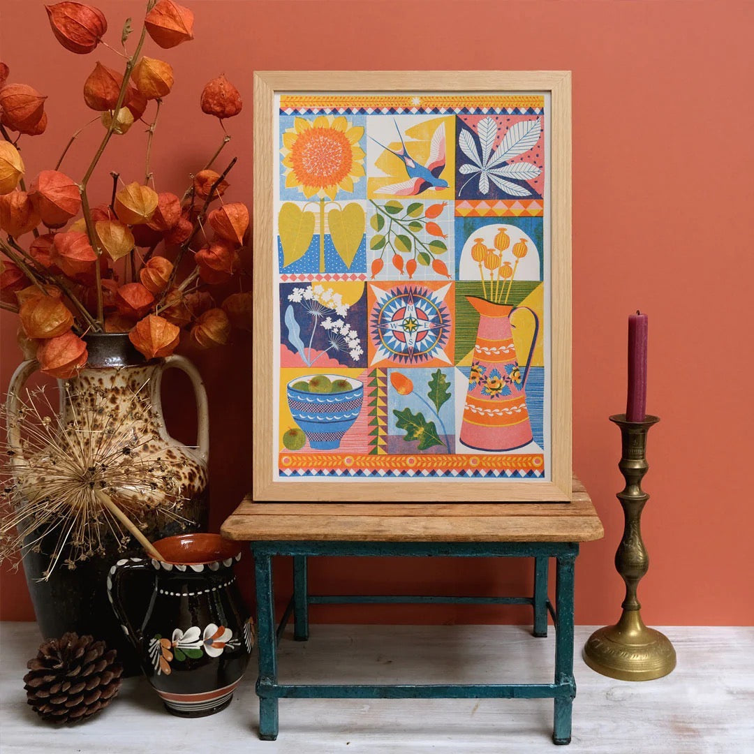 Colorful framed artwork on a wooden table with decorative items against an orange wall.