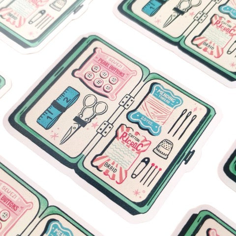 Sticker featuring an illustration of a sewing kit that includes needles, thread and scissors.