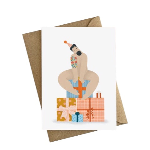 Birthday card featuring an illustration of a sexy, bearded, tattooed man sitting on top of a pile of birthday presents. 