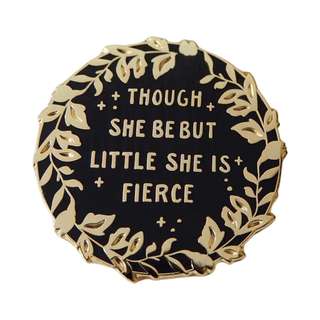 Circular enamel pin badge in black with gold foliage around the edges with the text 'And though she be but little, she is fierce' in gold in the centre. 
