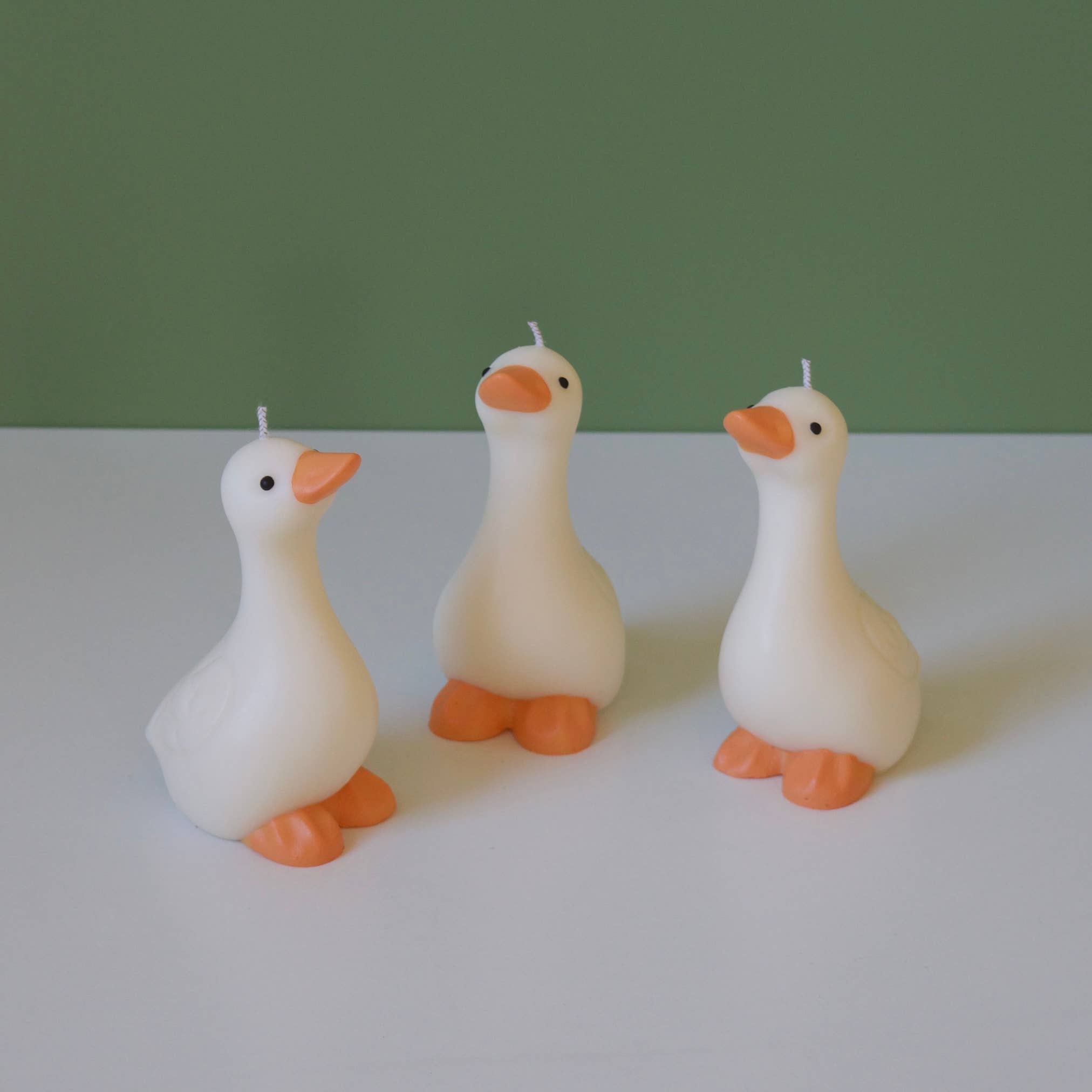 Three goose-shaped candles on a white surface with a green background.