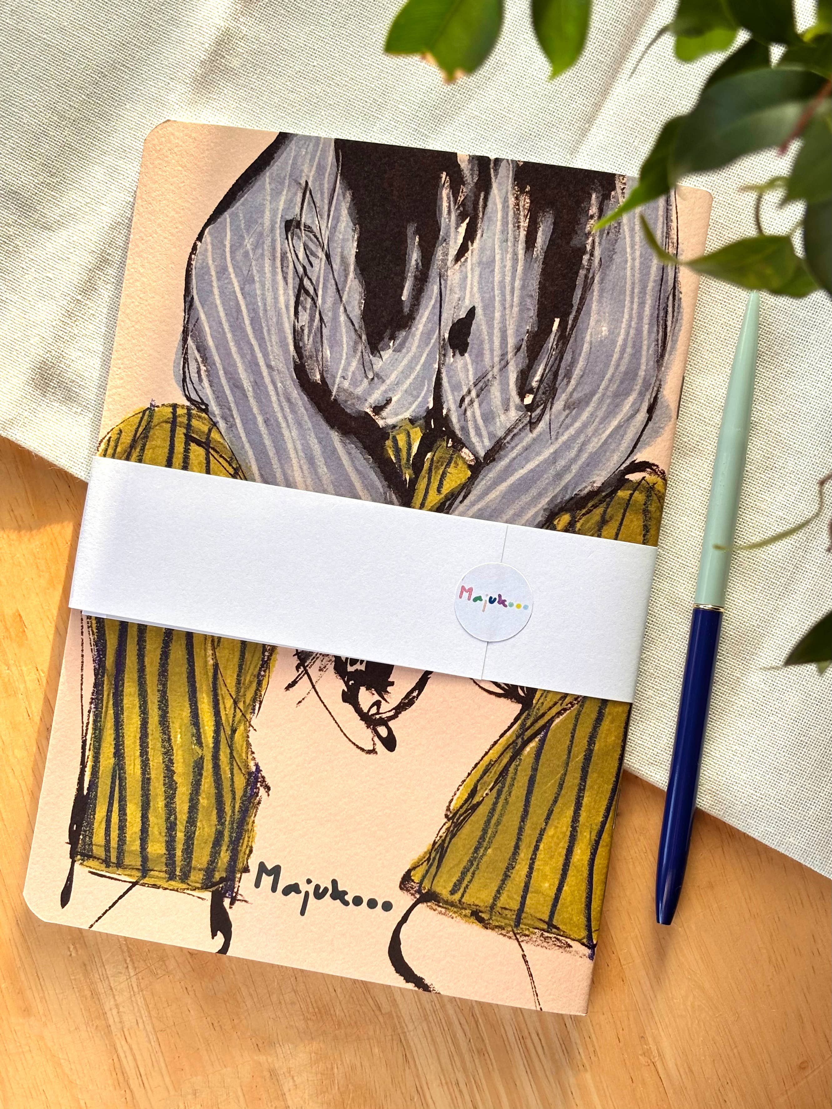 Packaged product with green trousers and a striped shirt and a pen on a wooden surface.