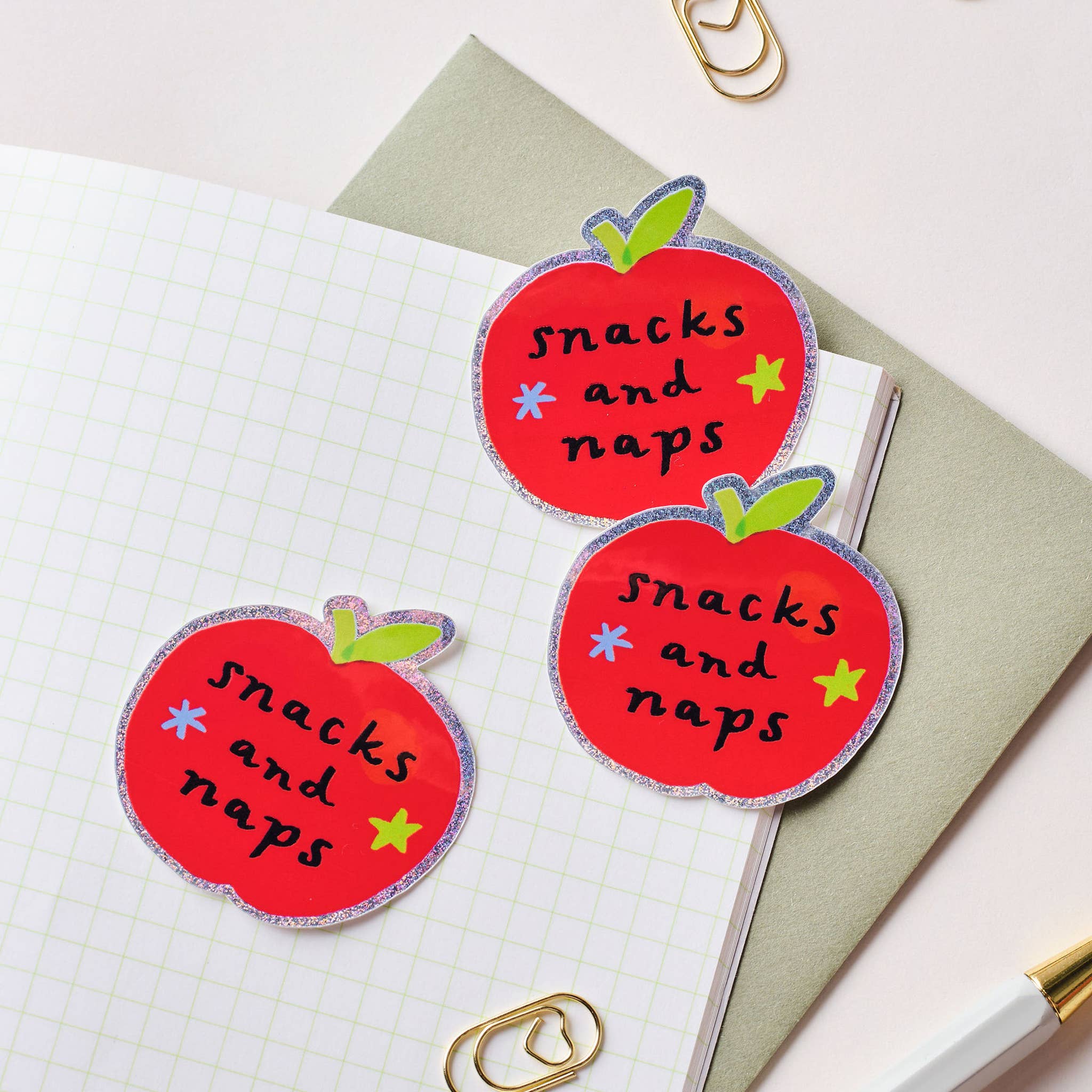 Three red apple-shaped stickers with 'snacks and naps' text on a notebook.