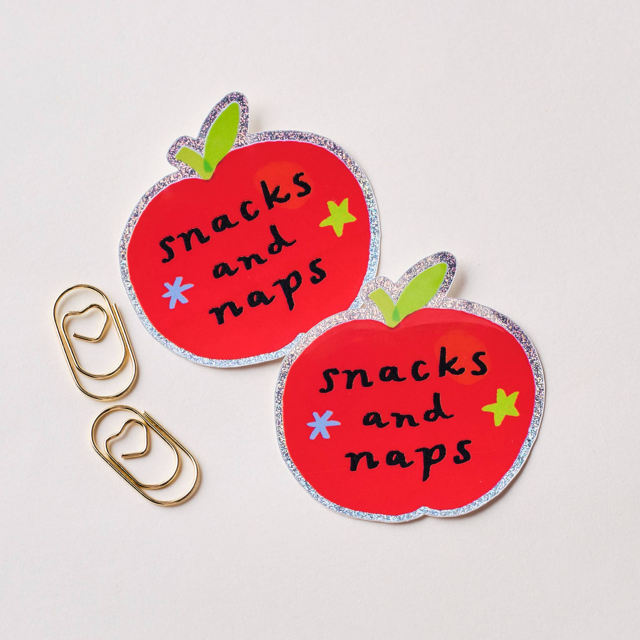 Two red apple-shaped stickers with 'snacks and naps' text on a light grey background.