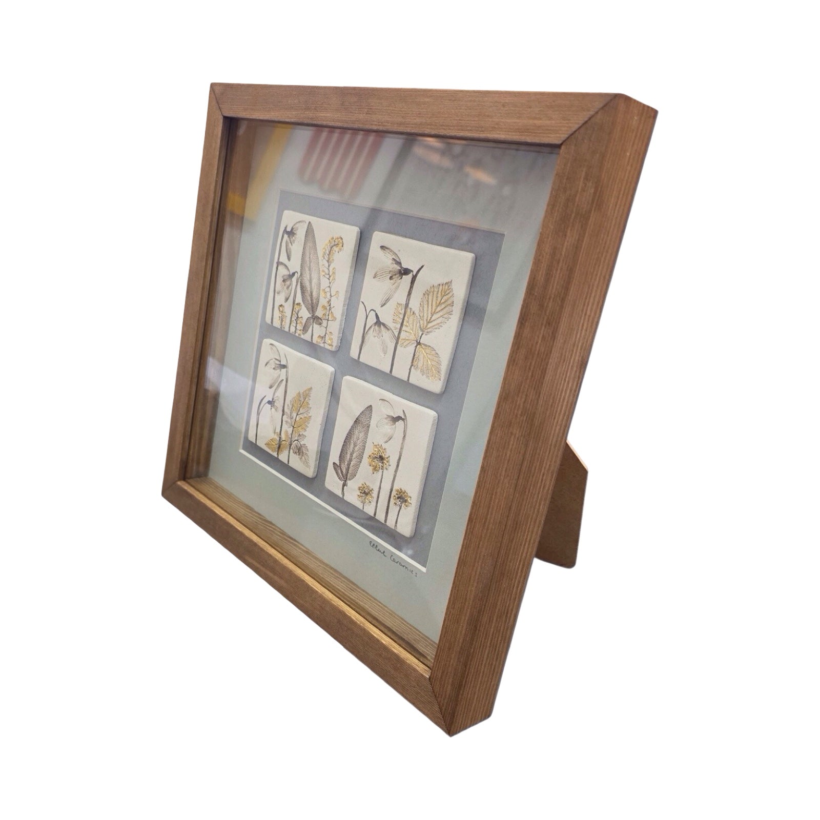 Framed artwork with four botanical tiles featuring snowdrops on a light grey background in an oak frame. 