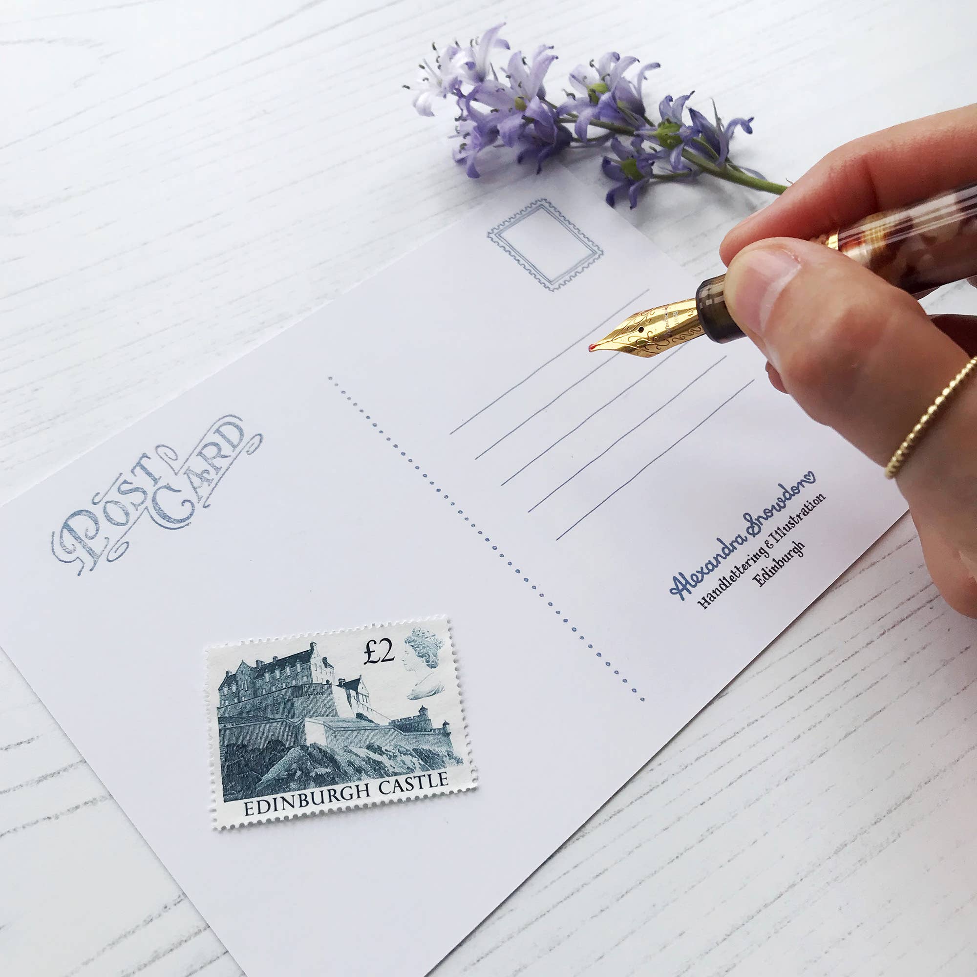 Hand writing on a postcard with a stamp and flower.