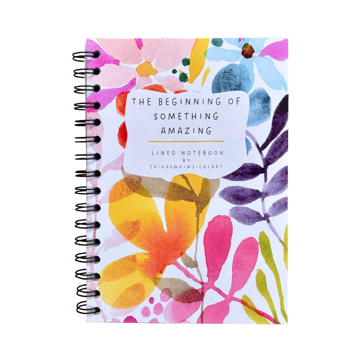 A spiral-bound lined notebook with a colourful watercolour floral cover, featuring a white label that reads 'THE BEGINNING OF SOMETHING AMAZING'.