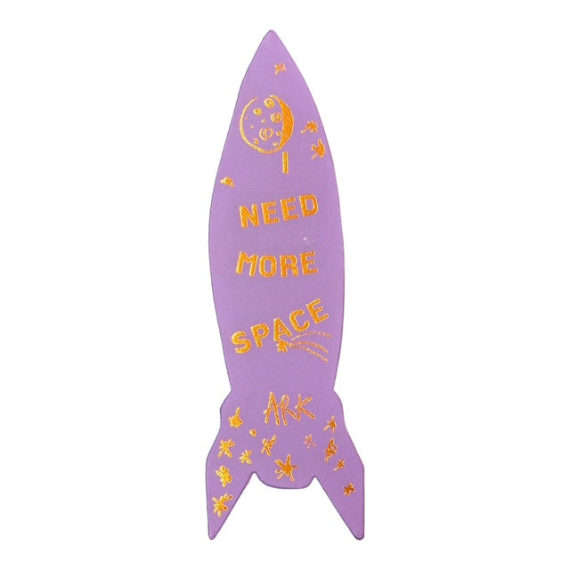 The lilac back of a space ship-shaped leather bookmark with the text 'I need more space' in gold writing.