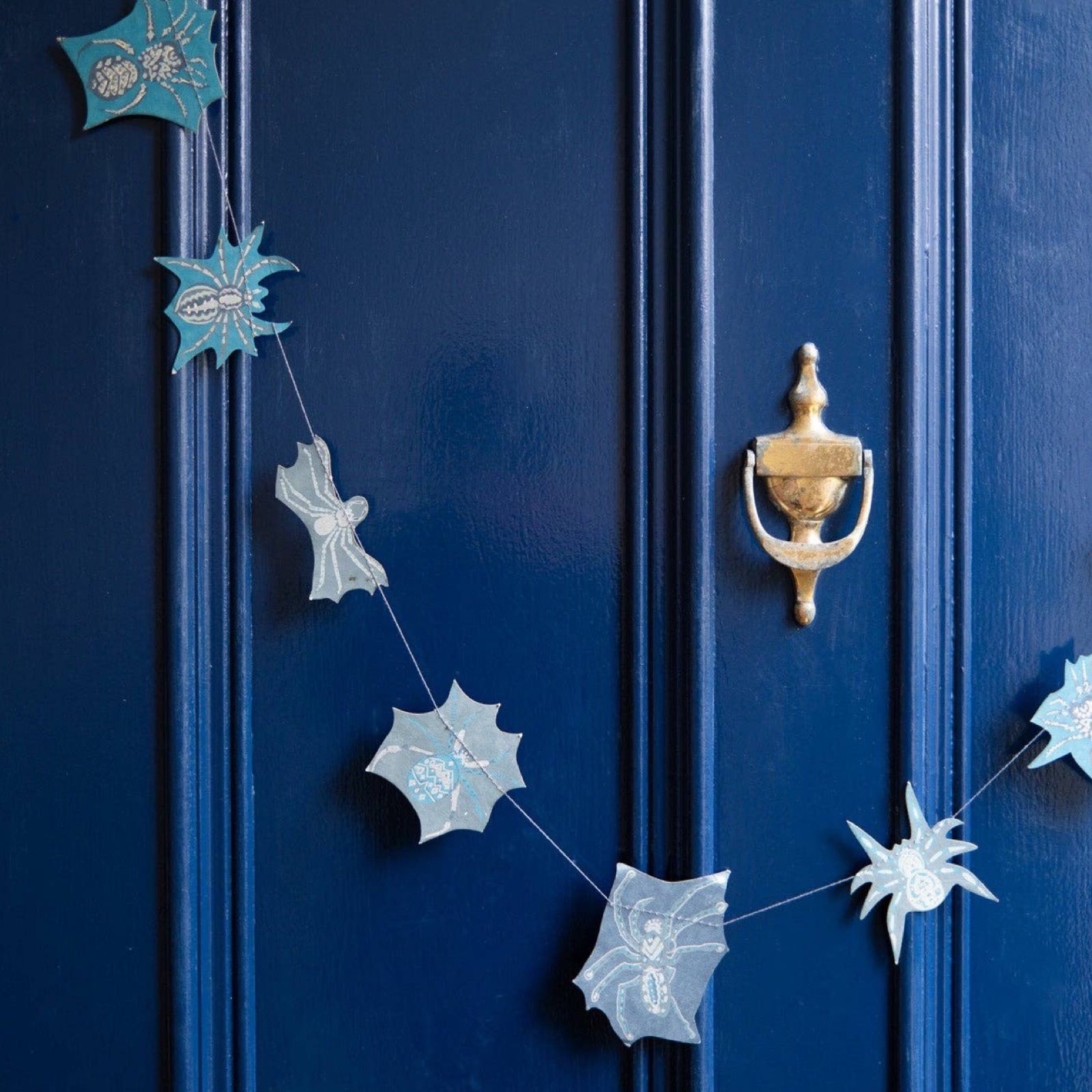 A spider paper garland with 20 screen printed spiders hanging on a blue door.