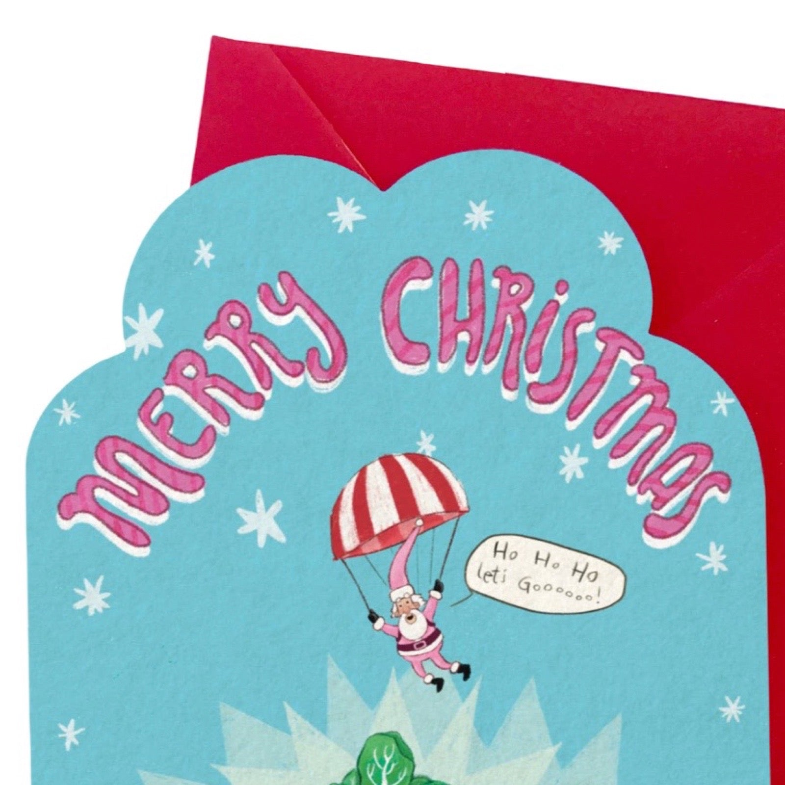 A Christmas greeting card with a bright blue scalloped front and a red envelope behind it. The card says “Merry Christmas” in pink letters and shows Santa Claus parachuting down with a red-and-white striped parachute.