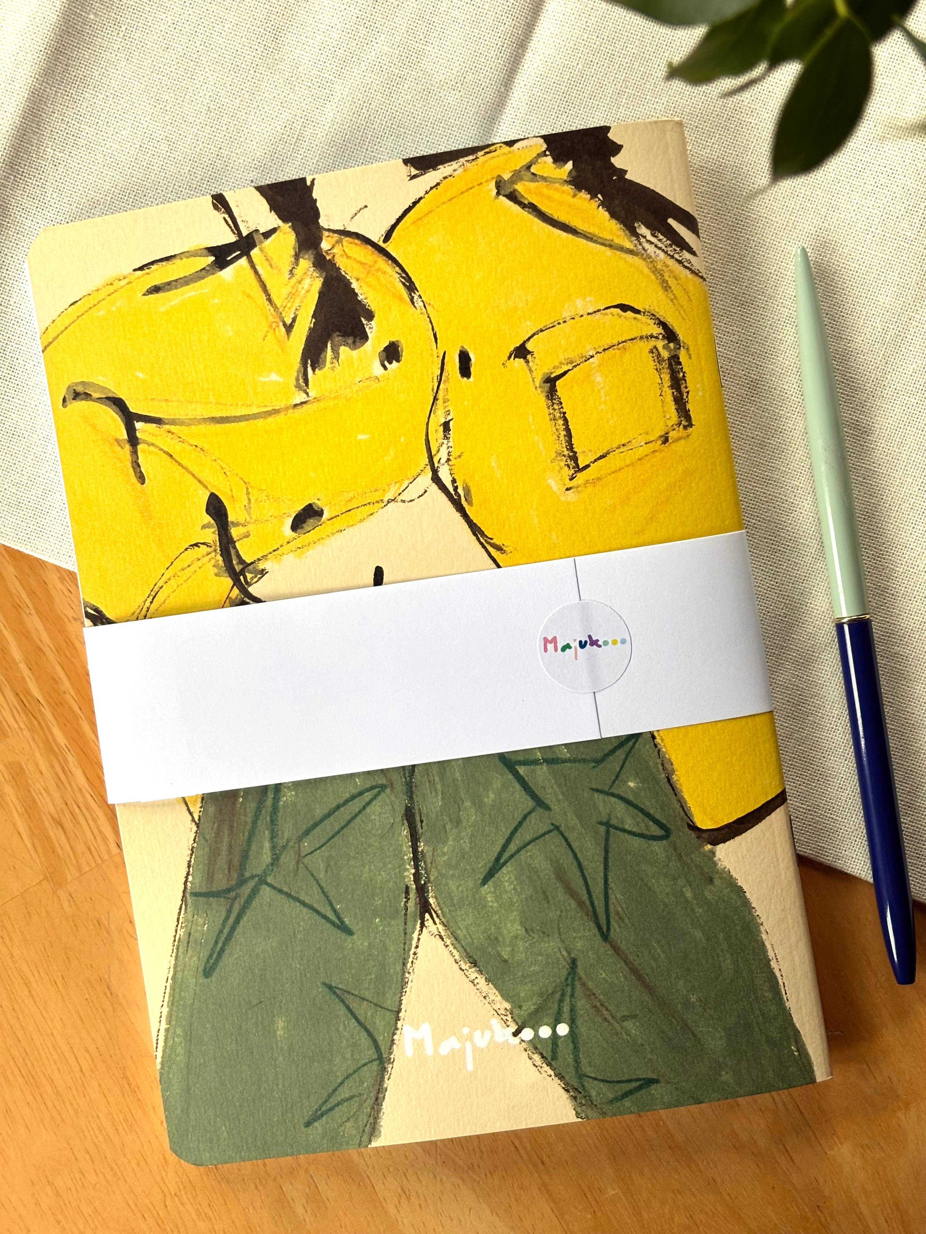 Notebook with yellow and green design on a wooden surface with a pen.
