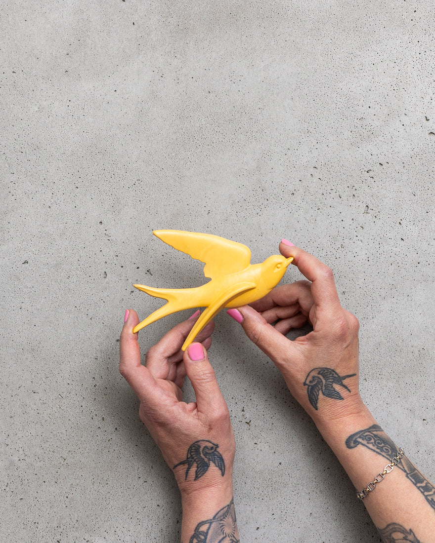 Yellow bird figurine held by hands on a grey concrete surface.