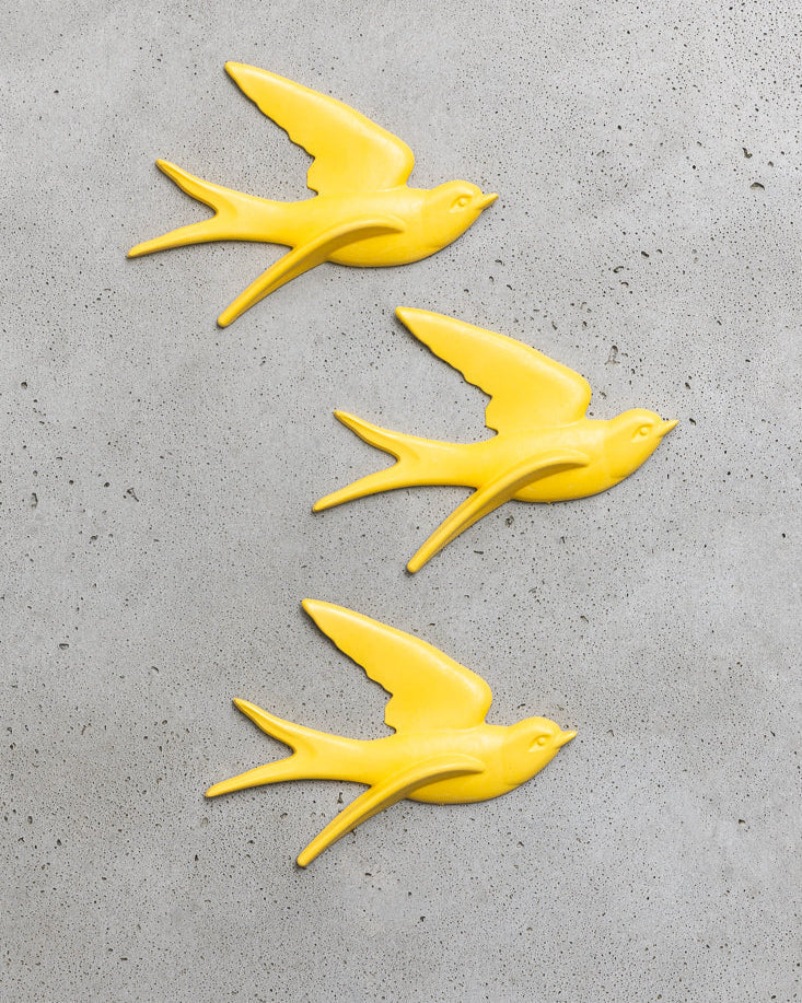Three yellow bird-shaped decorations on a grey concrete surface.