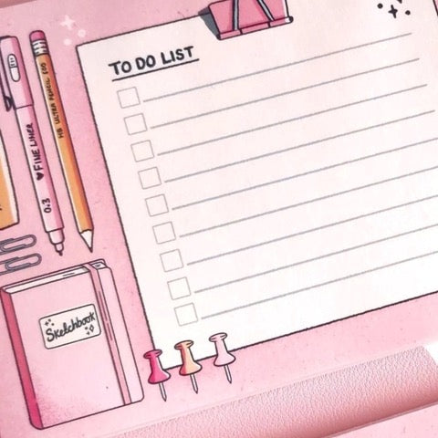 A to-do list pad and a notepad all in one surrounded by stationery items such as a box of pencils and a highlighter all against a pale pink background.