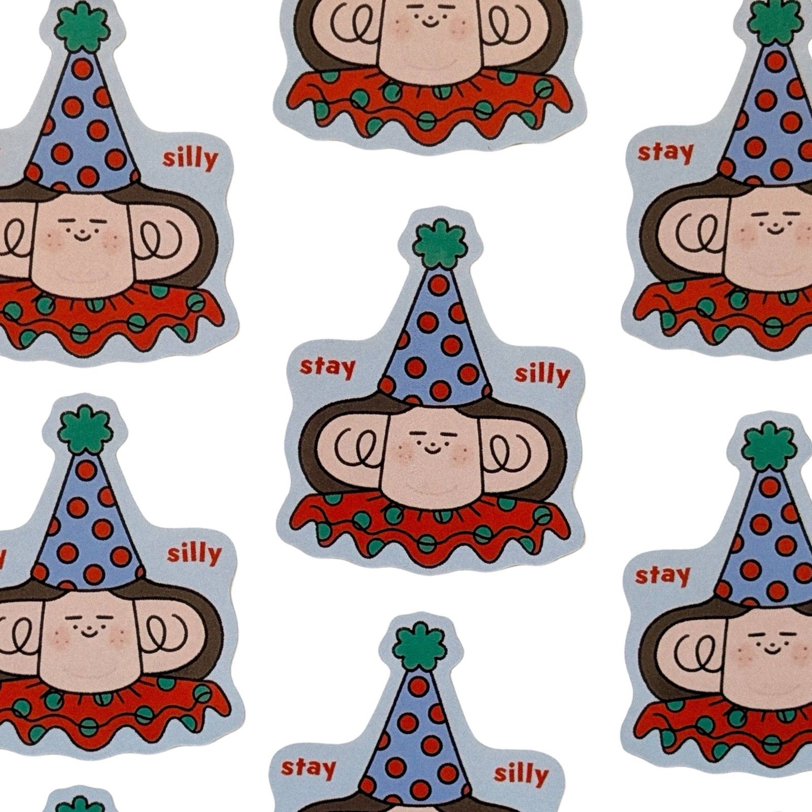 A repeating pattern of cartoon faces wearing party hats with the words 'stay silly' on a white background.