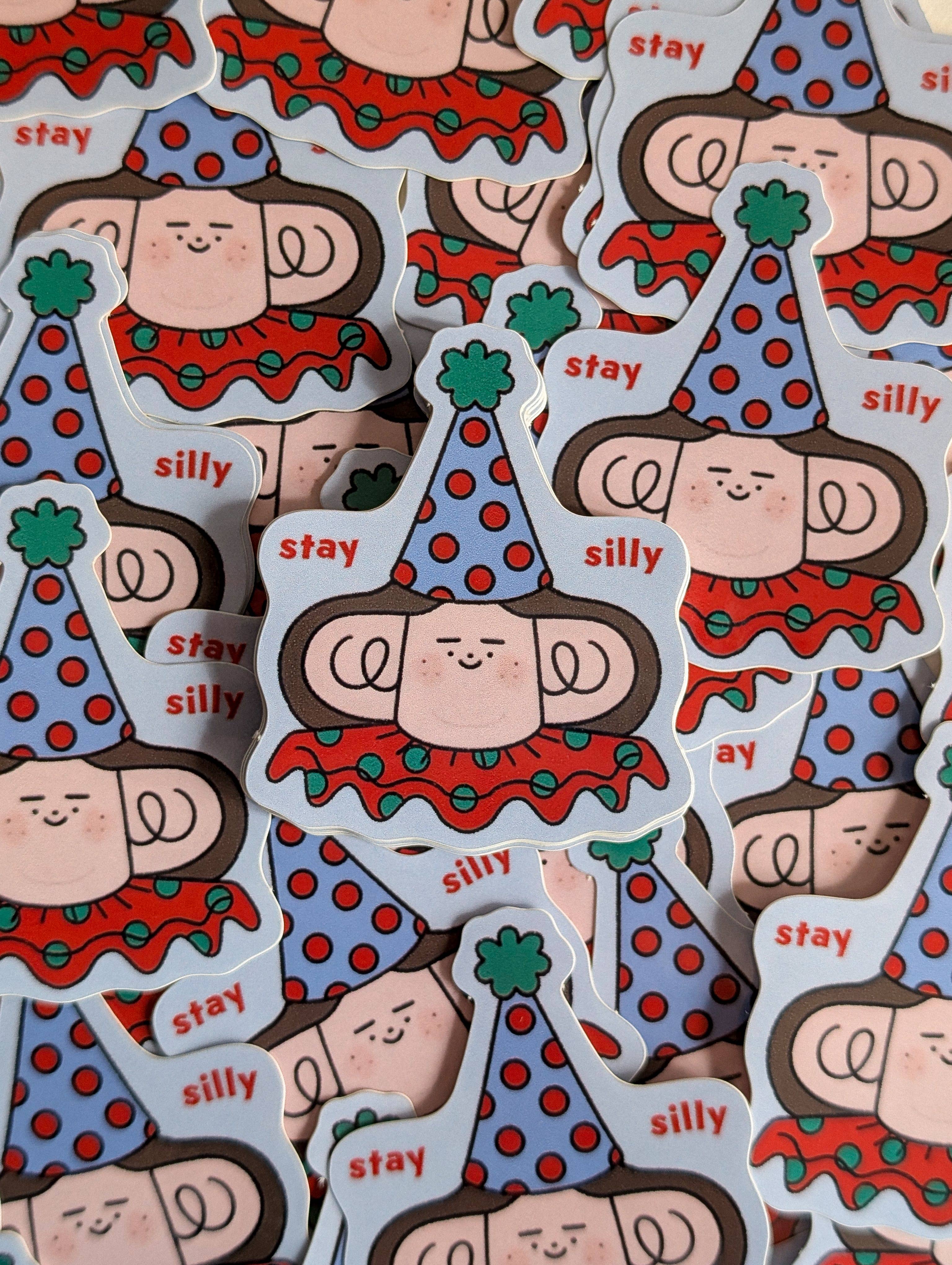 A pile of die-cut stickers featuring a cartoon character with a blue polka-dot party hat, red patterned top, and the words 'stay' and 'silly' in red text.