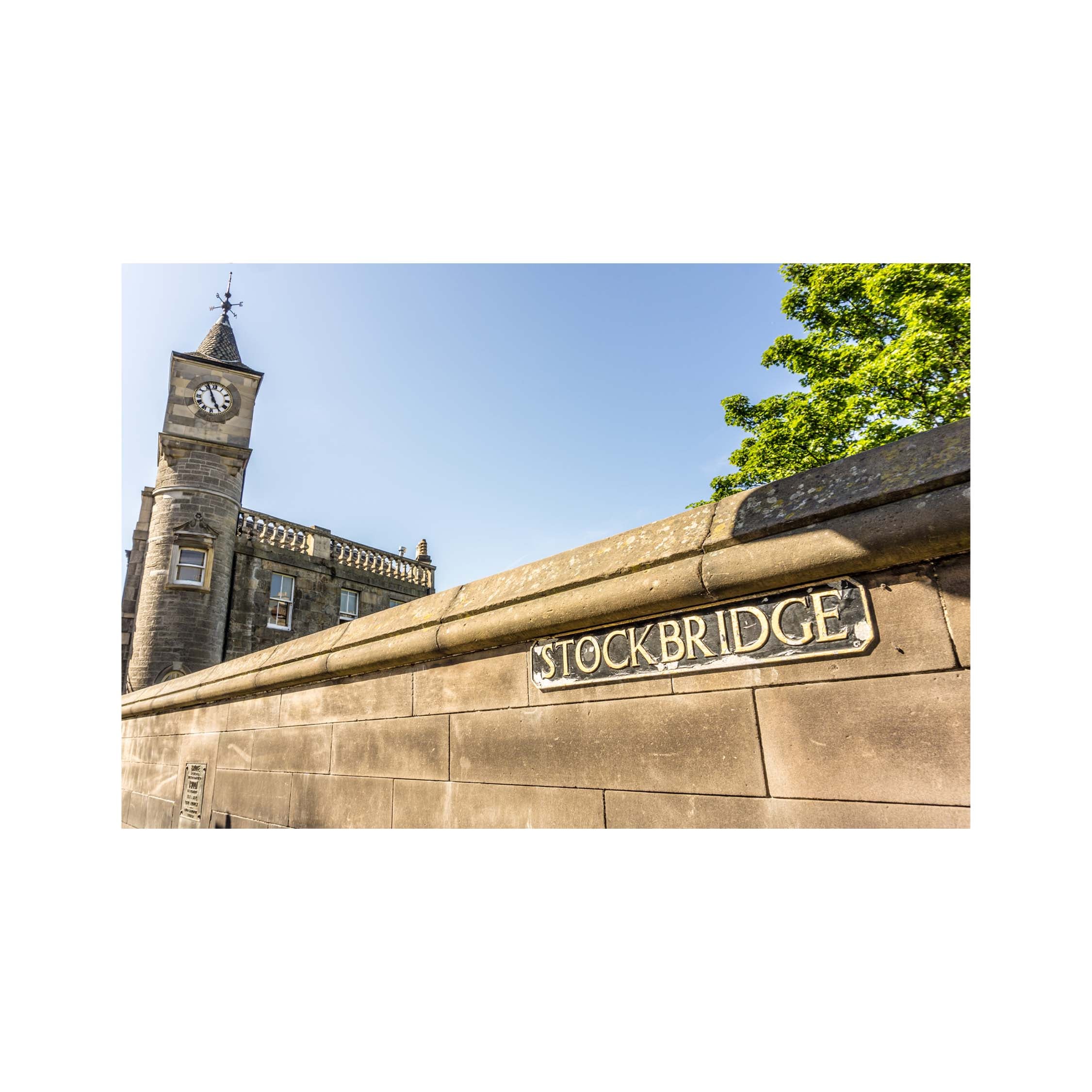 Stone wall with 'Stockbridge' sign and clock tower in the background
