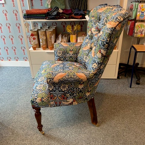 A hand-crafted occasional armchair covered in William Morris-inspired strawberry thief fabric, with a button-back and cream binding, mahogany legs, and gold castors.