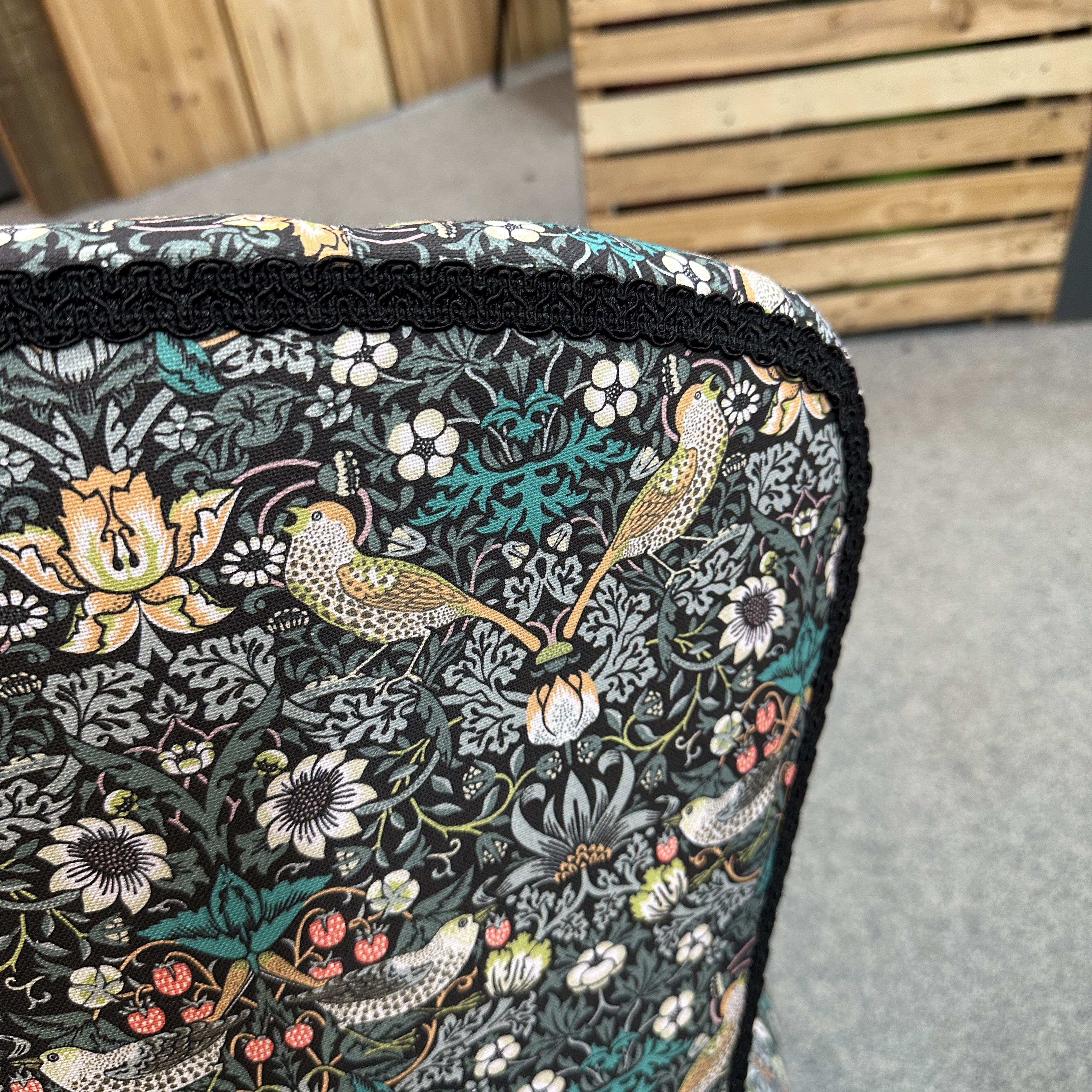 Floral and bird patterned chair on a wooden and grey floor background.