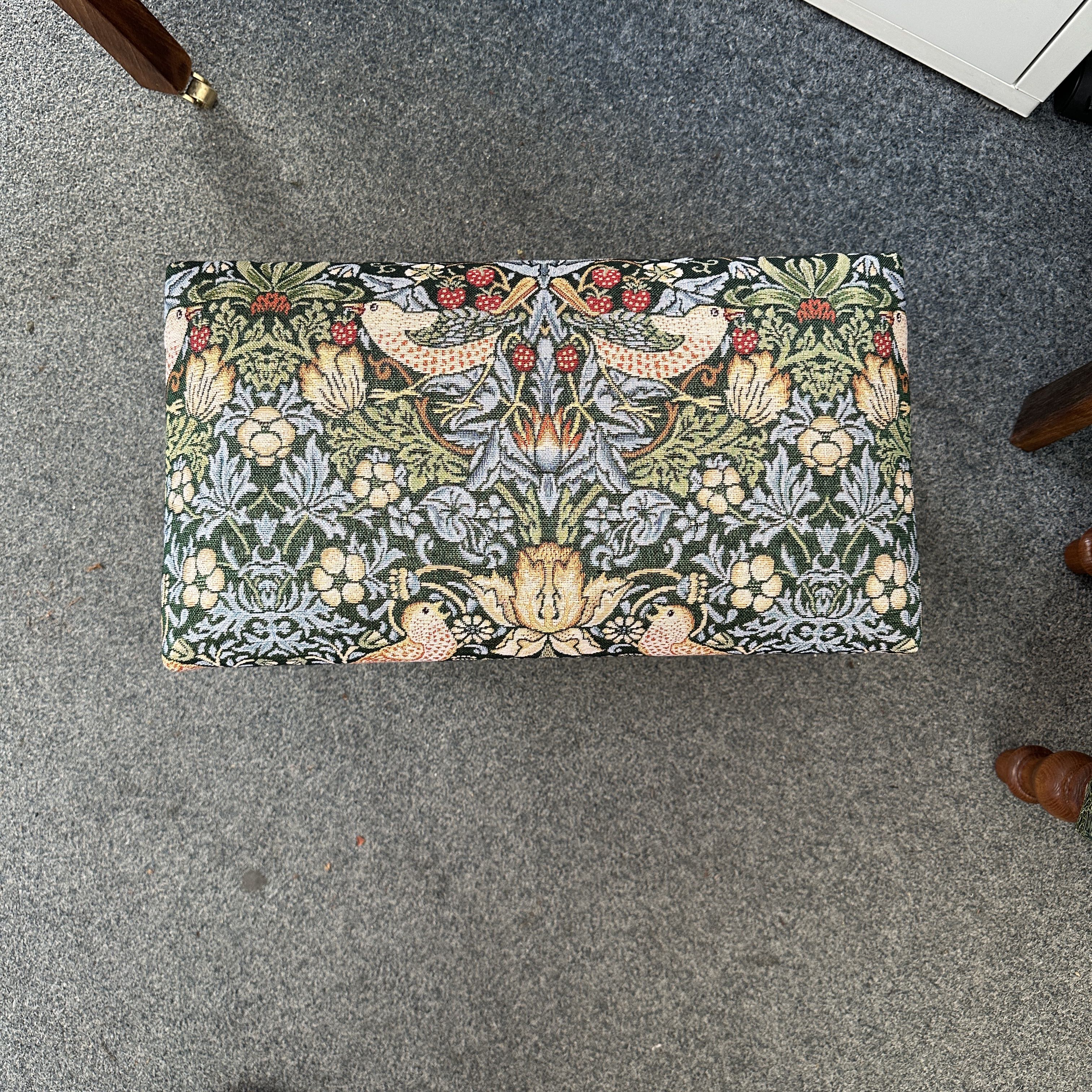 Decorative footstool with floral and bird pattern on a gray floor.
