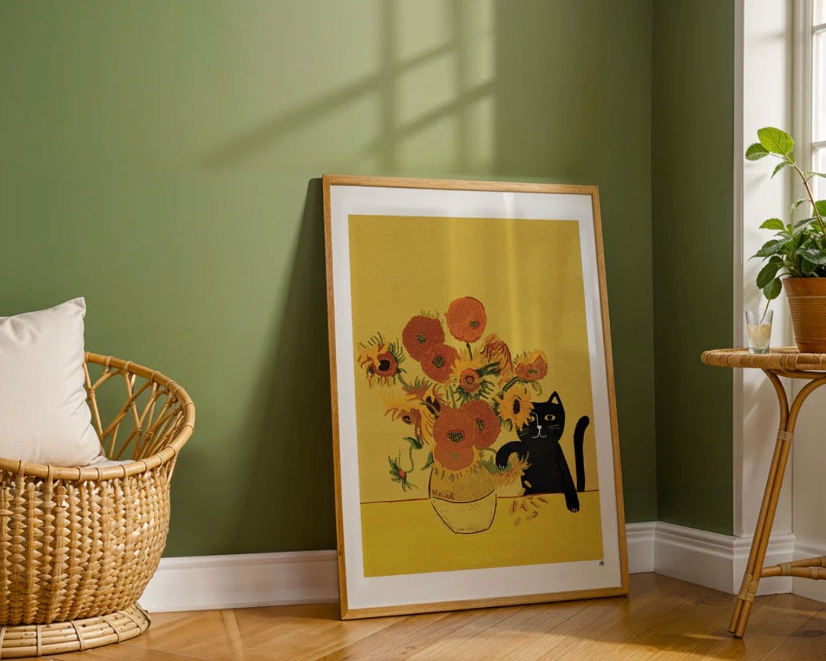 Framed artwork of a cat and flowers on a green wall with a wicker chair and plant.