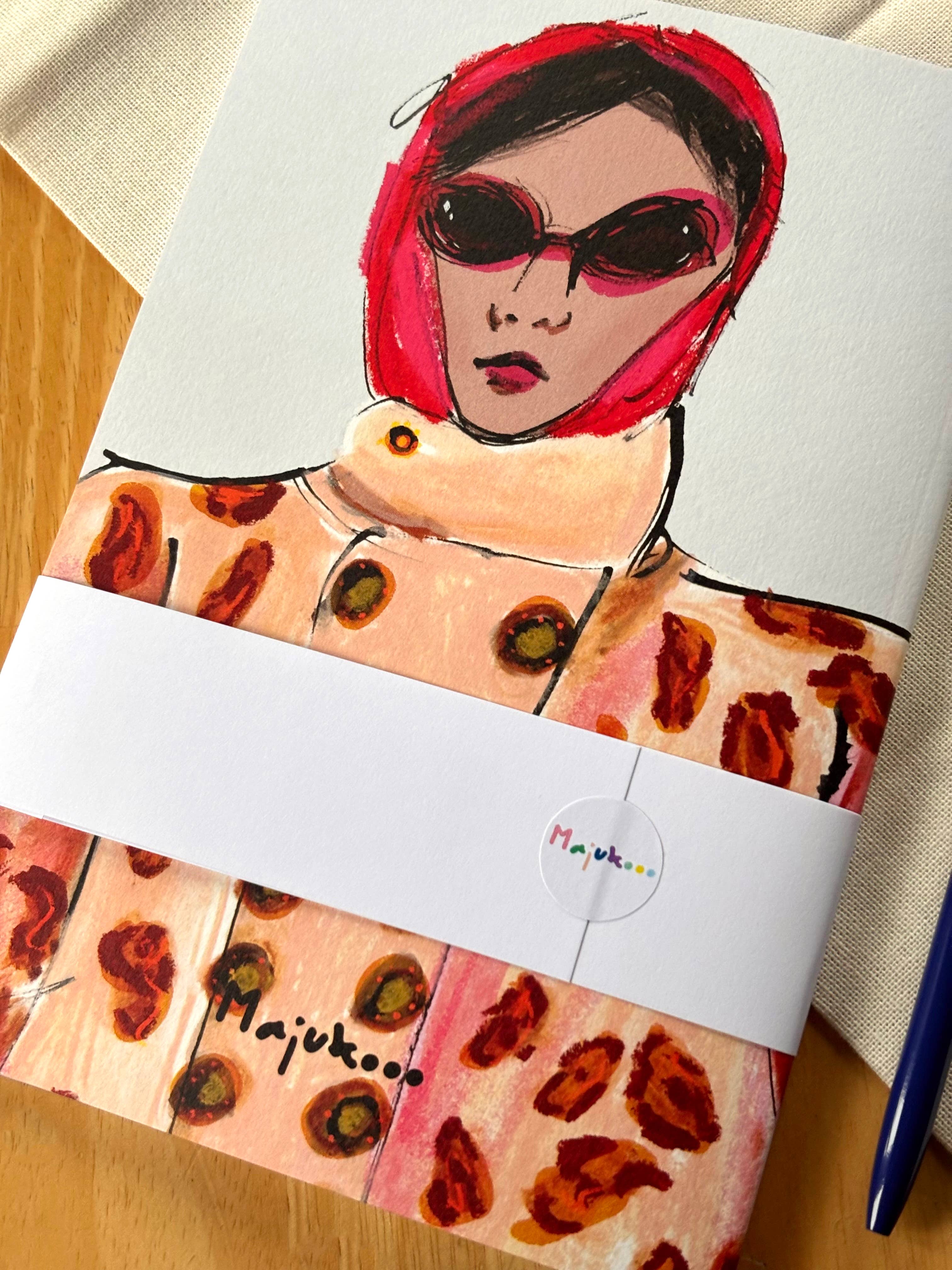 Packaged product with artistic design of a person with red hair and sunglasses, featuring the brand 'Majukoo'.