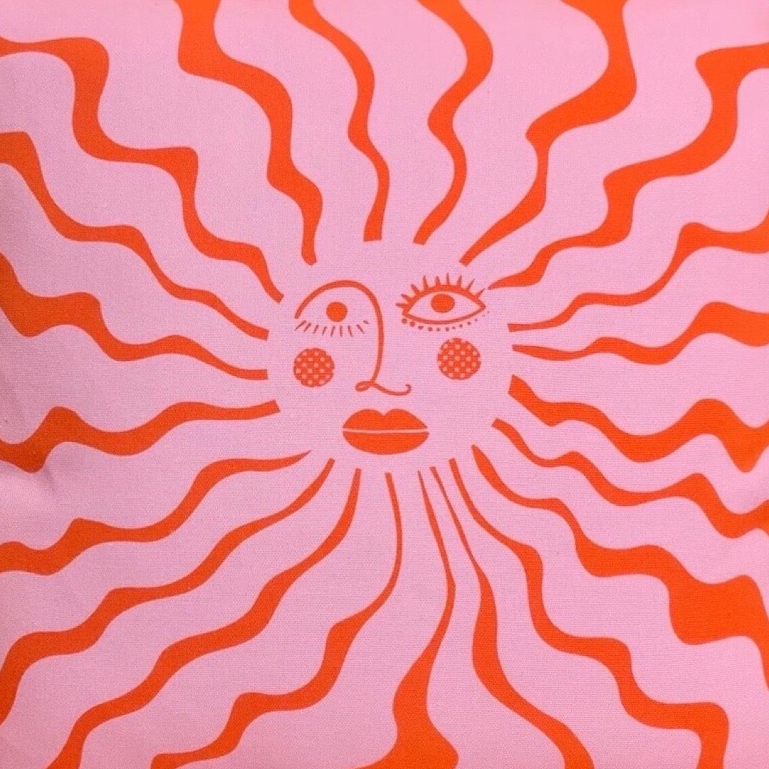 A fabulous pink cushion cover with an illustration of the sun with a face in red.