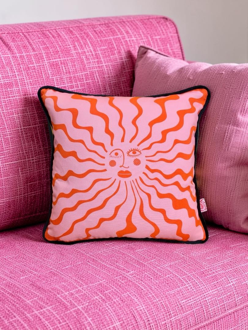 Decorative cushion with sun design on a pink couch.