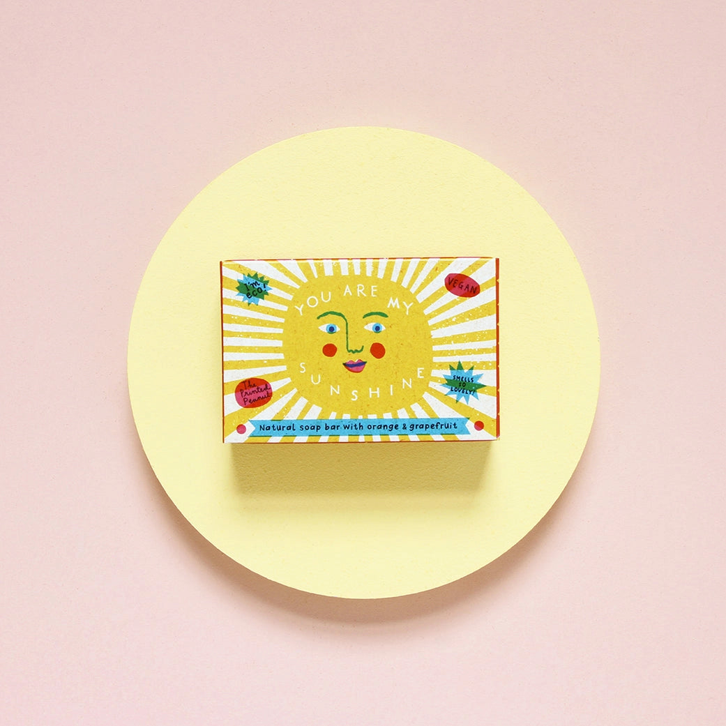 Soap bar with an illustration of a sun, sat on a yellow soap dish.