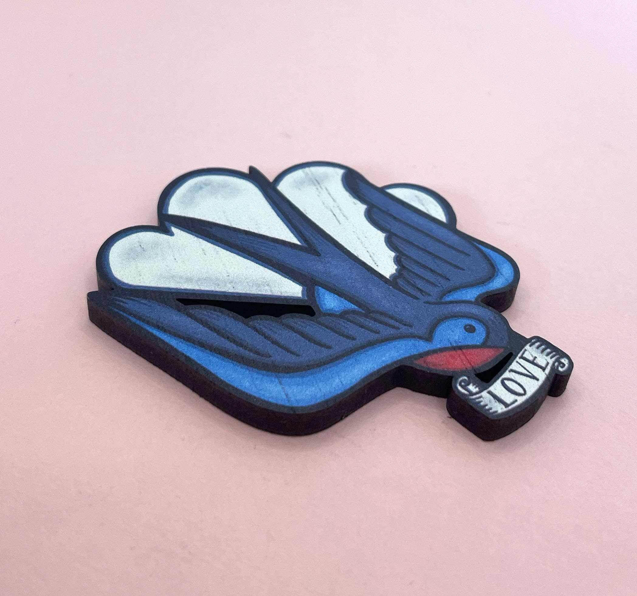 Blue dove brooch with 'Love' message on a pink background.