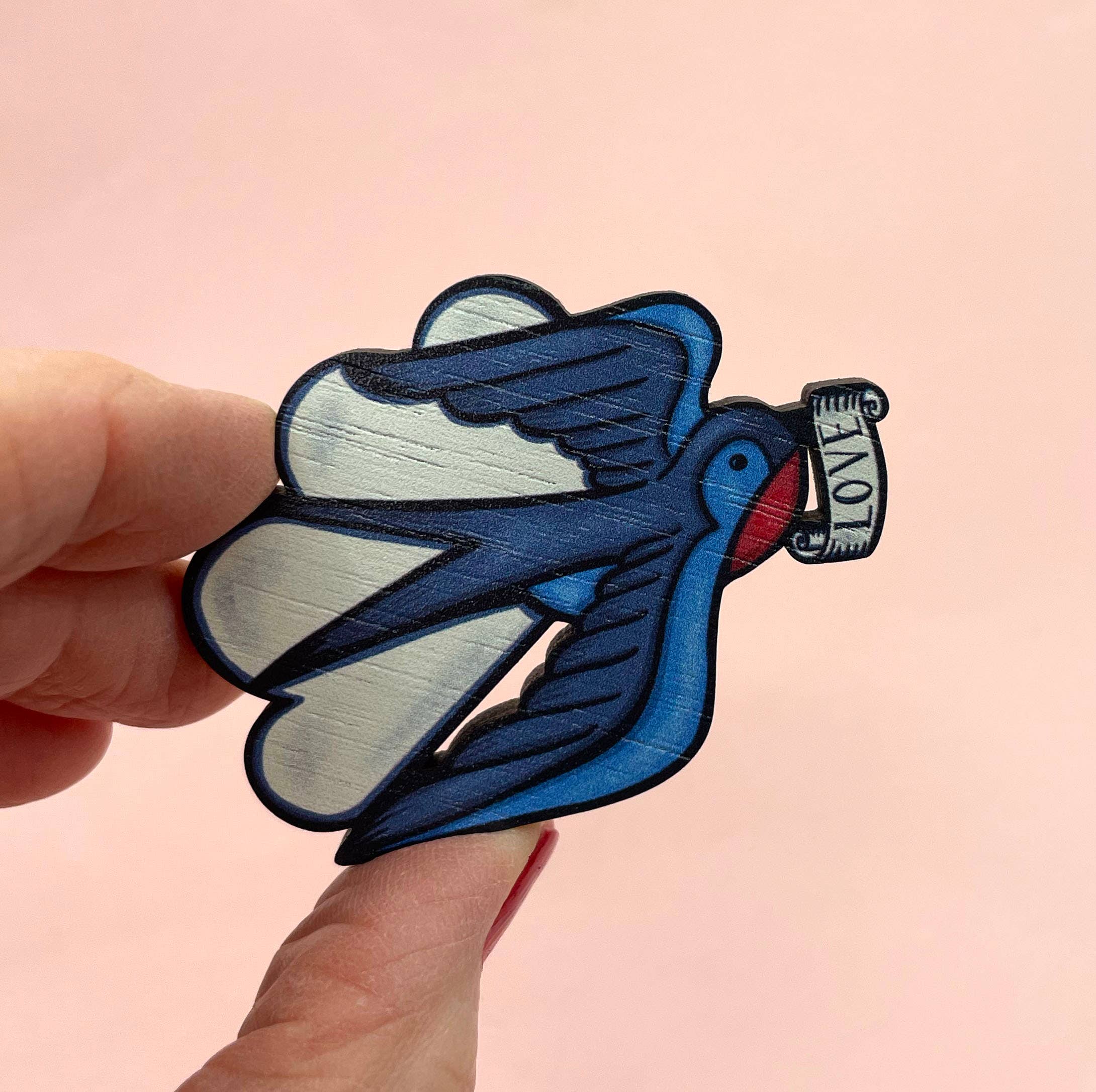 Blue swallow brooch held by a hand against a pink background.