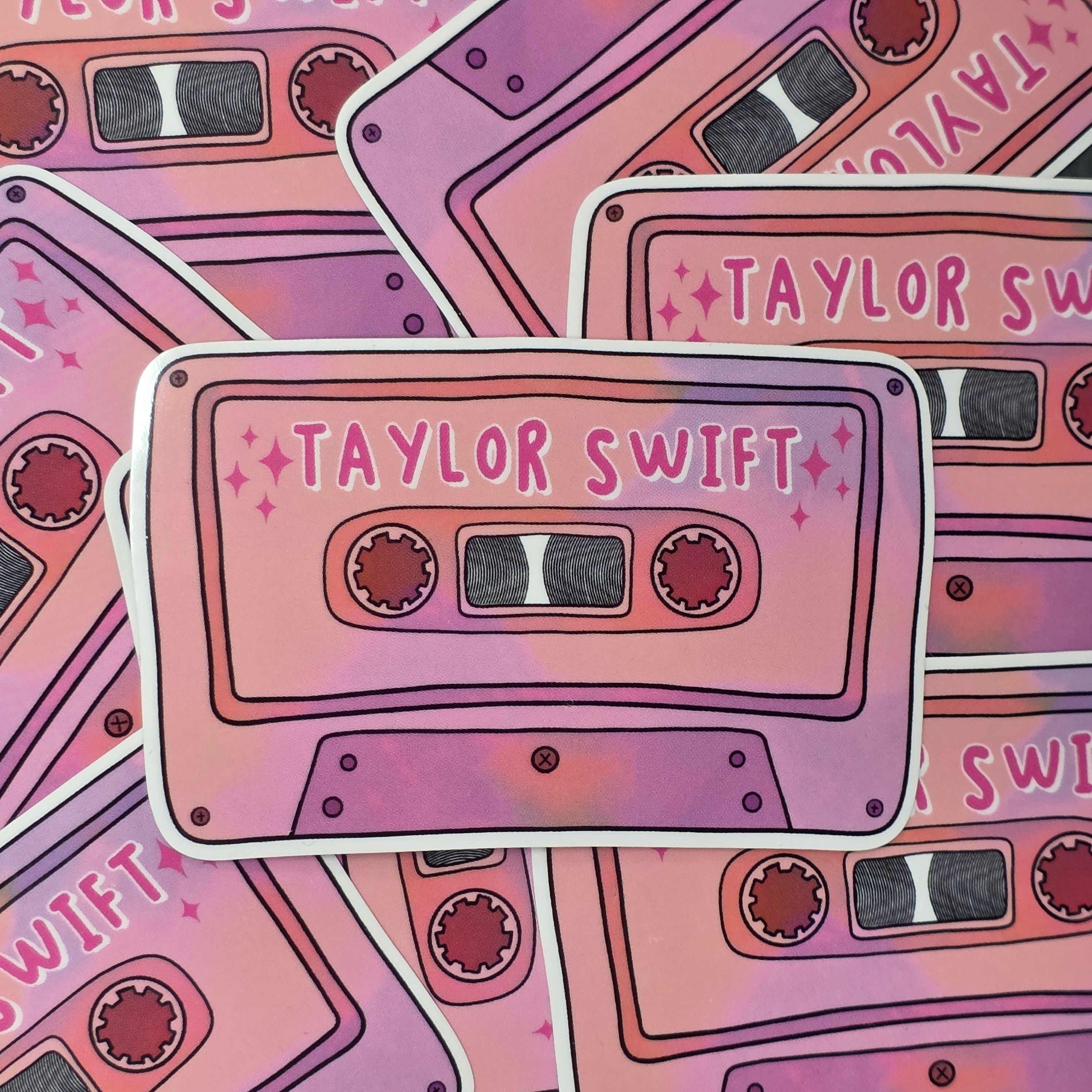 A rectangular-shaped sticker featuring an illustration of a retro cassette tape in dark and light pink with the title 'Taylor Swift'.