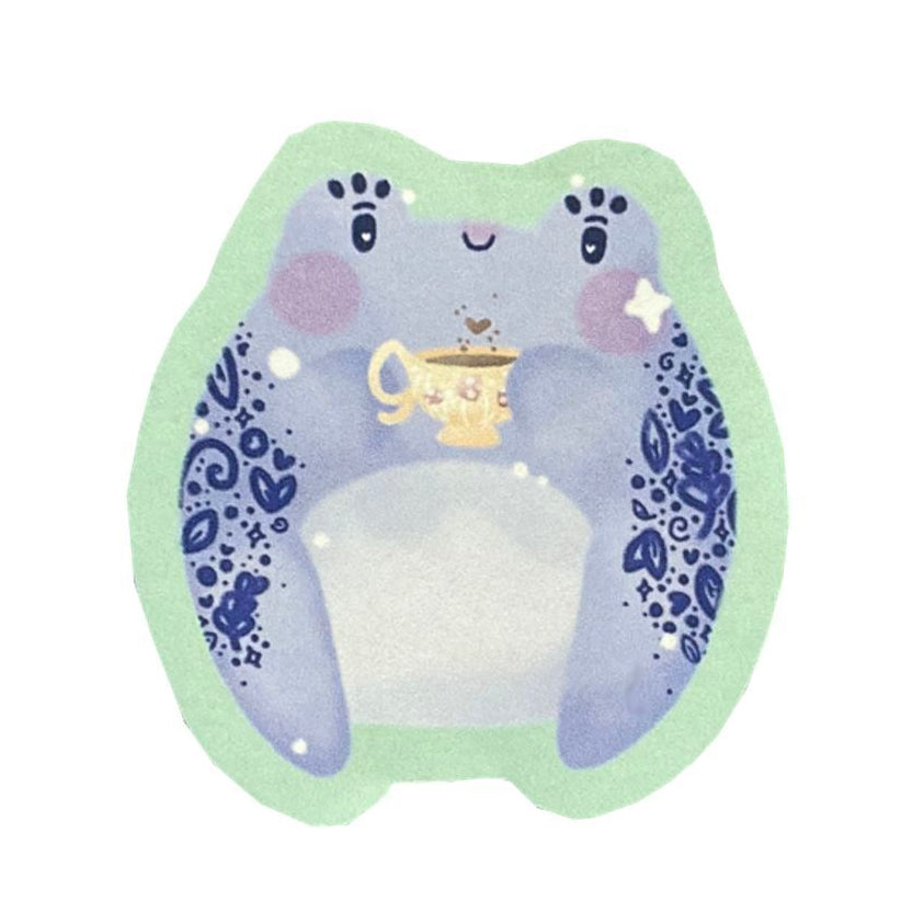 Photo of a sticker of a blue frog holding a yellow cup of tea