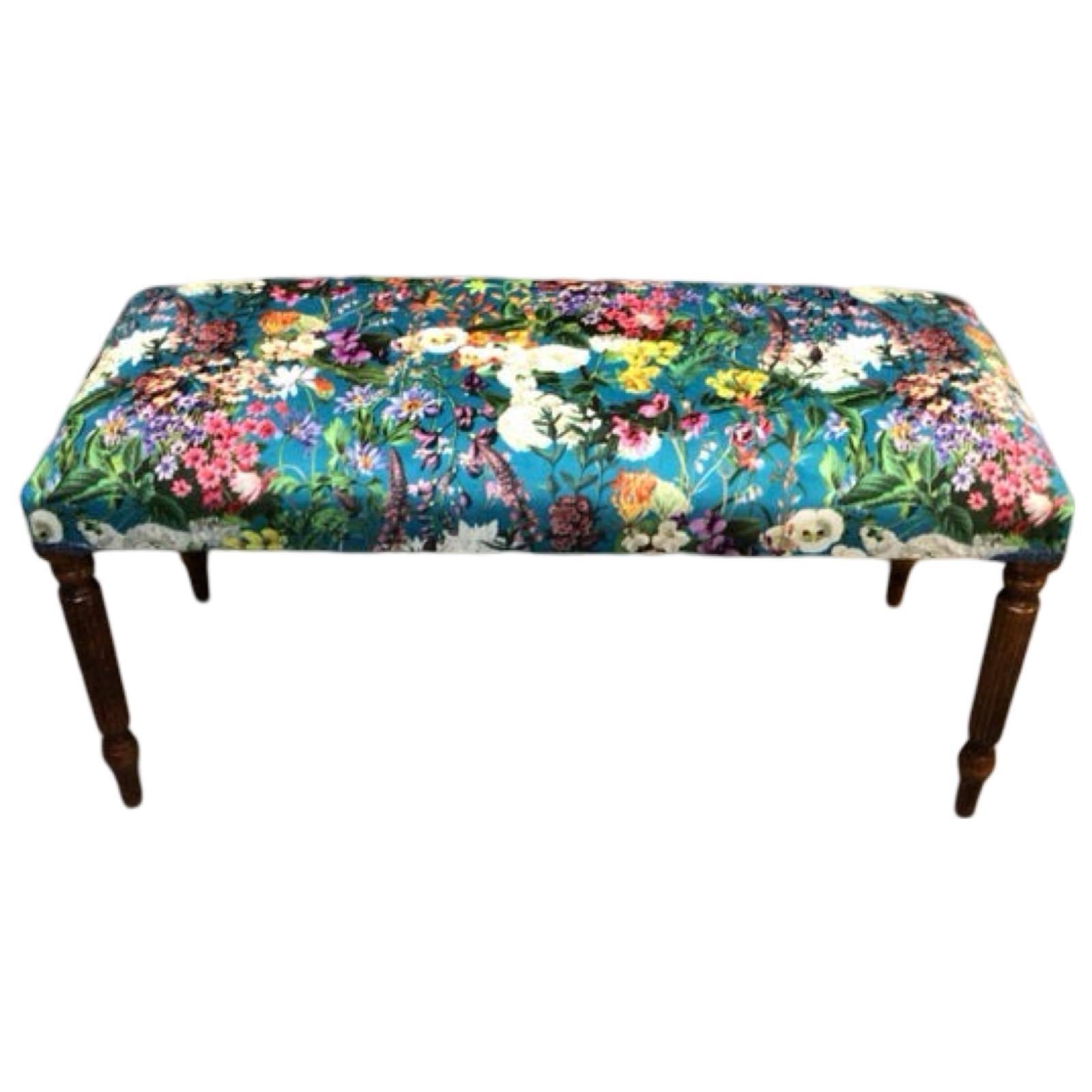 A rectangular bench with mahogany legs and a luxurious velvet fabric upholstery featuring a bright colourful floral design.