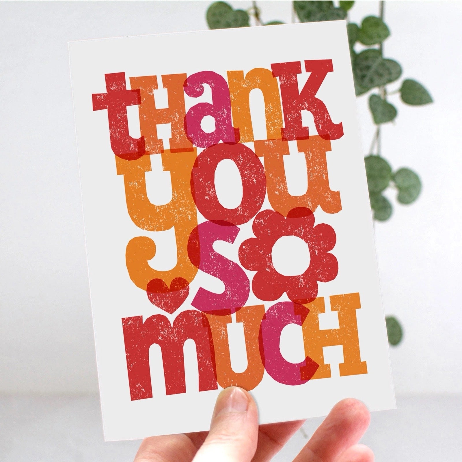 Card with 'Thank you so much' text in colourful letters held by a hand against a light background.