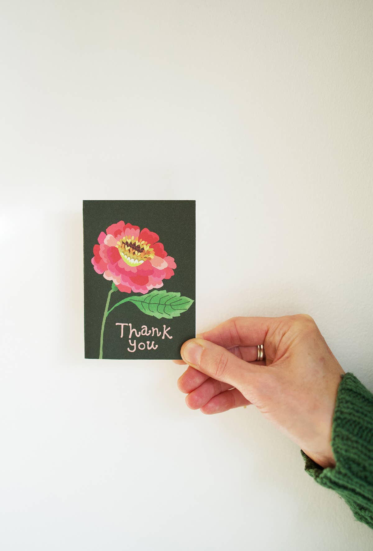 Hand holding a small card with a pink flower and 'Thank you' text on a white background.