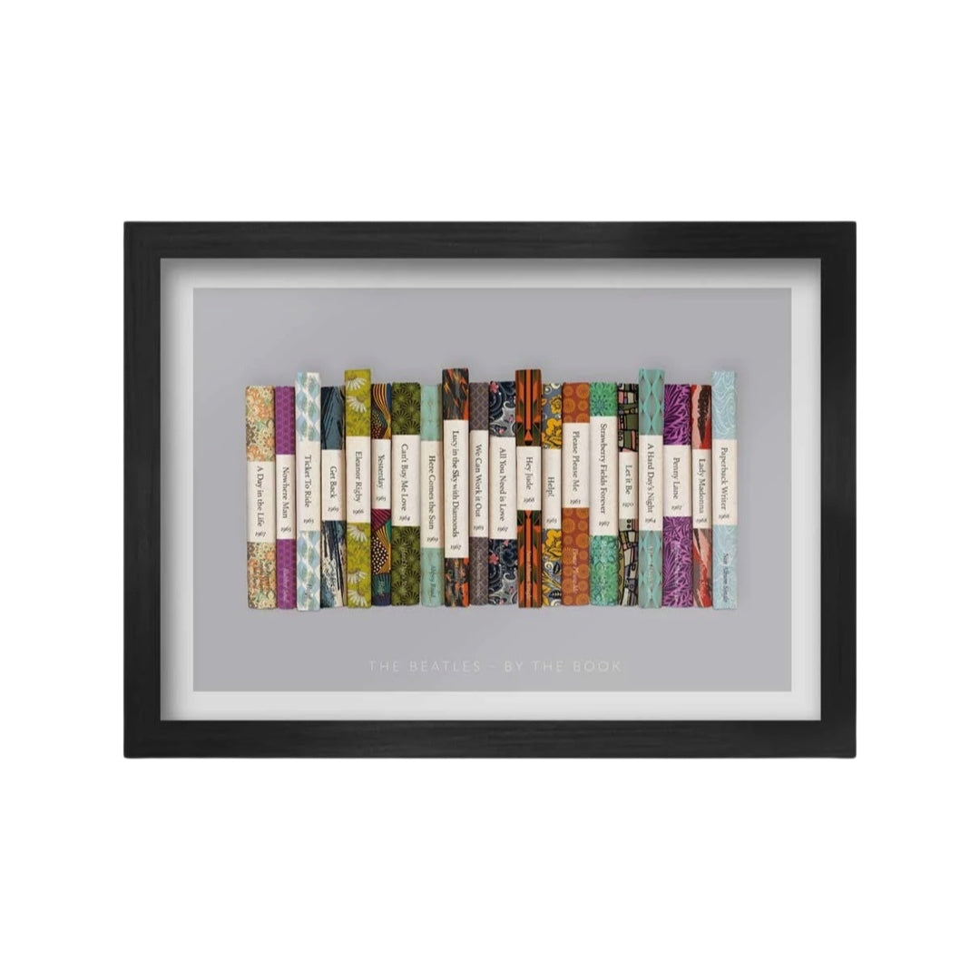 A framed A3 print featuring a stack of books with spine designs representing The Beatles' songs, displayed on a gray background.