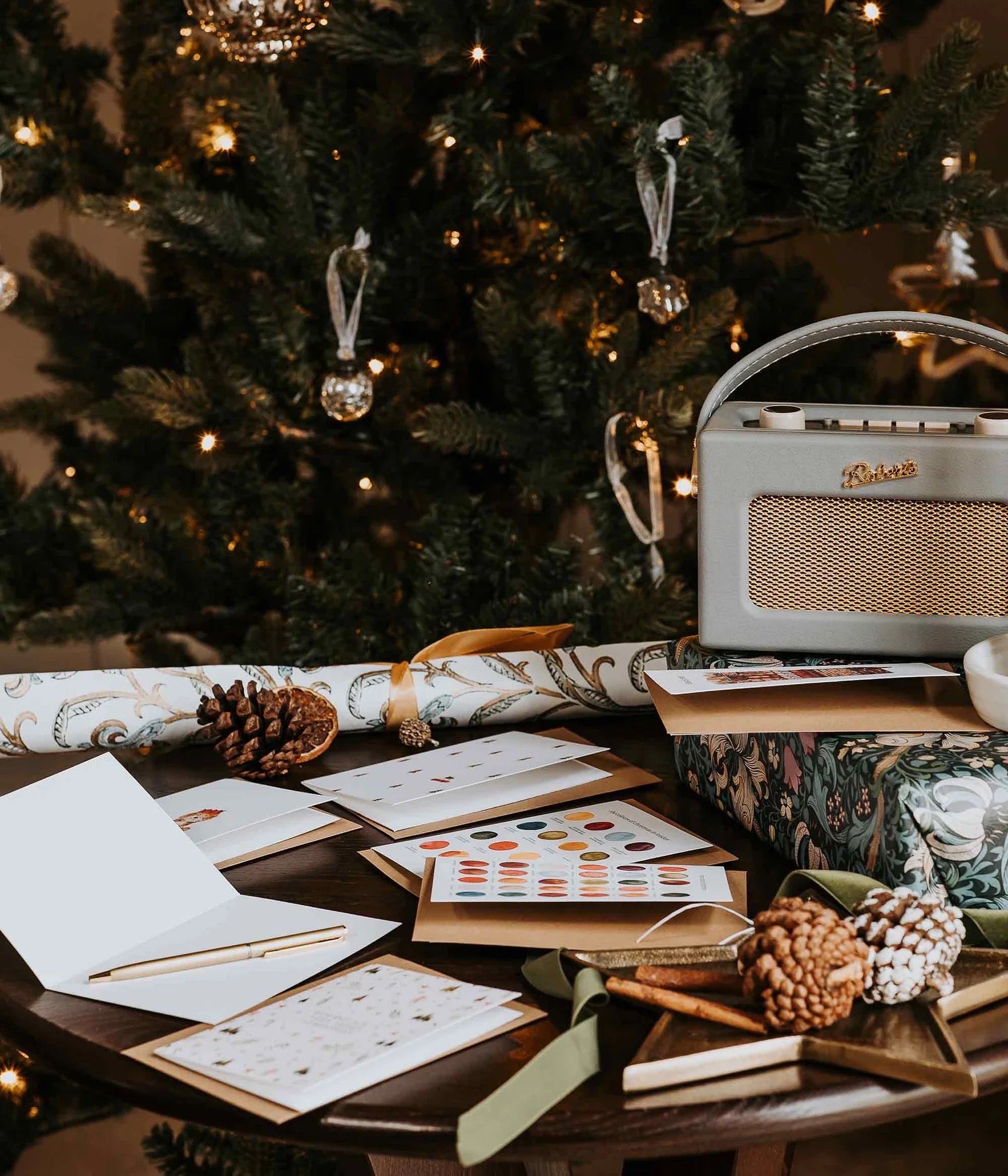 Table with Christmas cards, stationery, and a radio in front of a decorated tree.