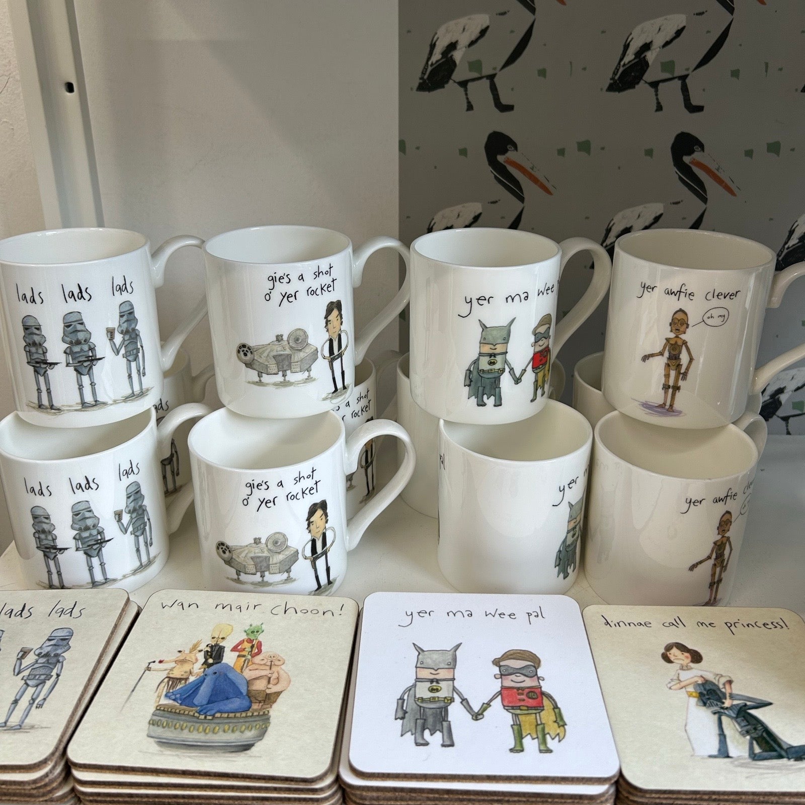 Set of mugs and coasters with illustrated designs on a shelf.
