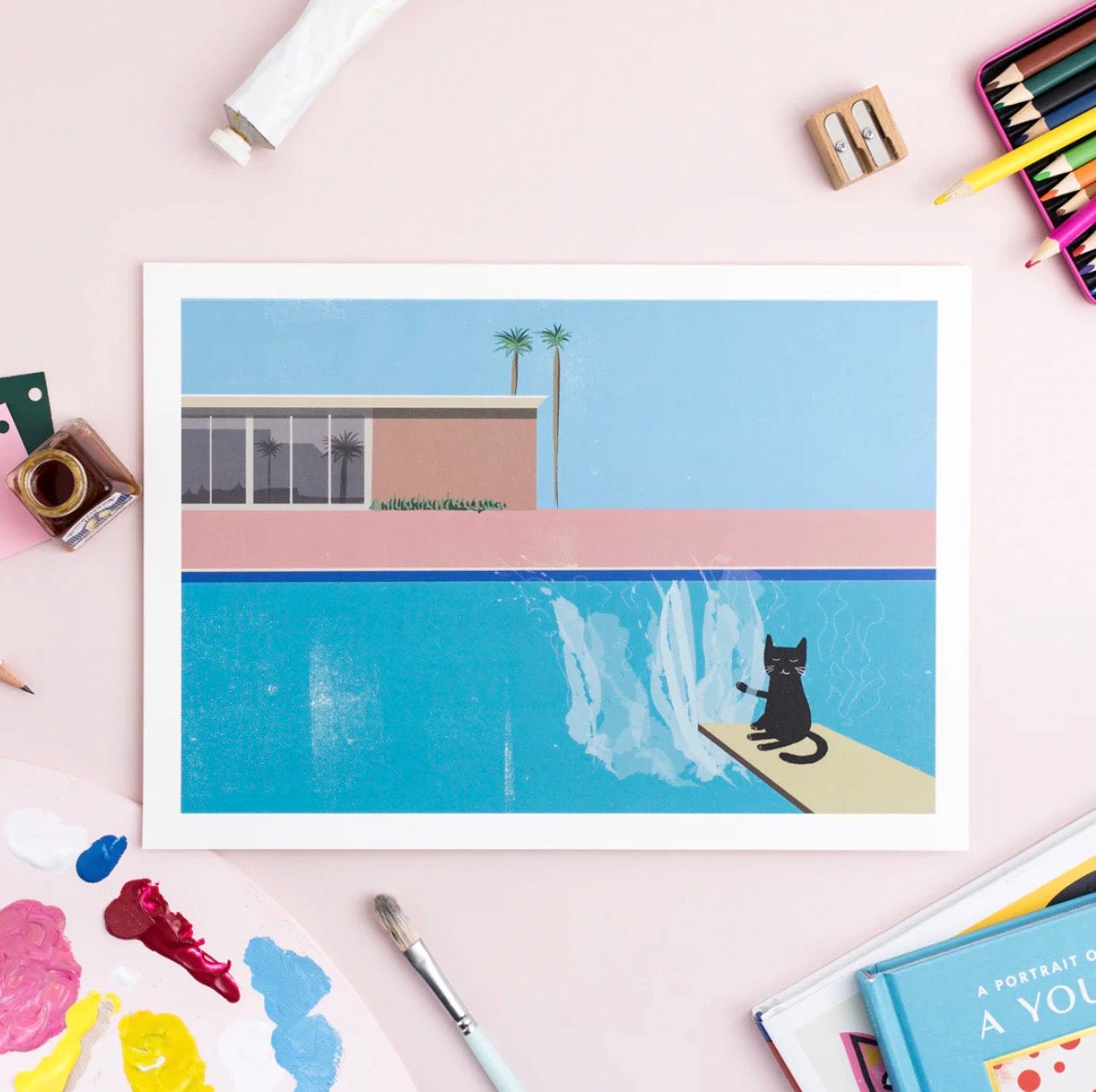 Framed artwork of a cat by a pool with art supplies around.