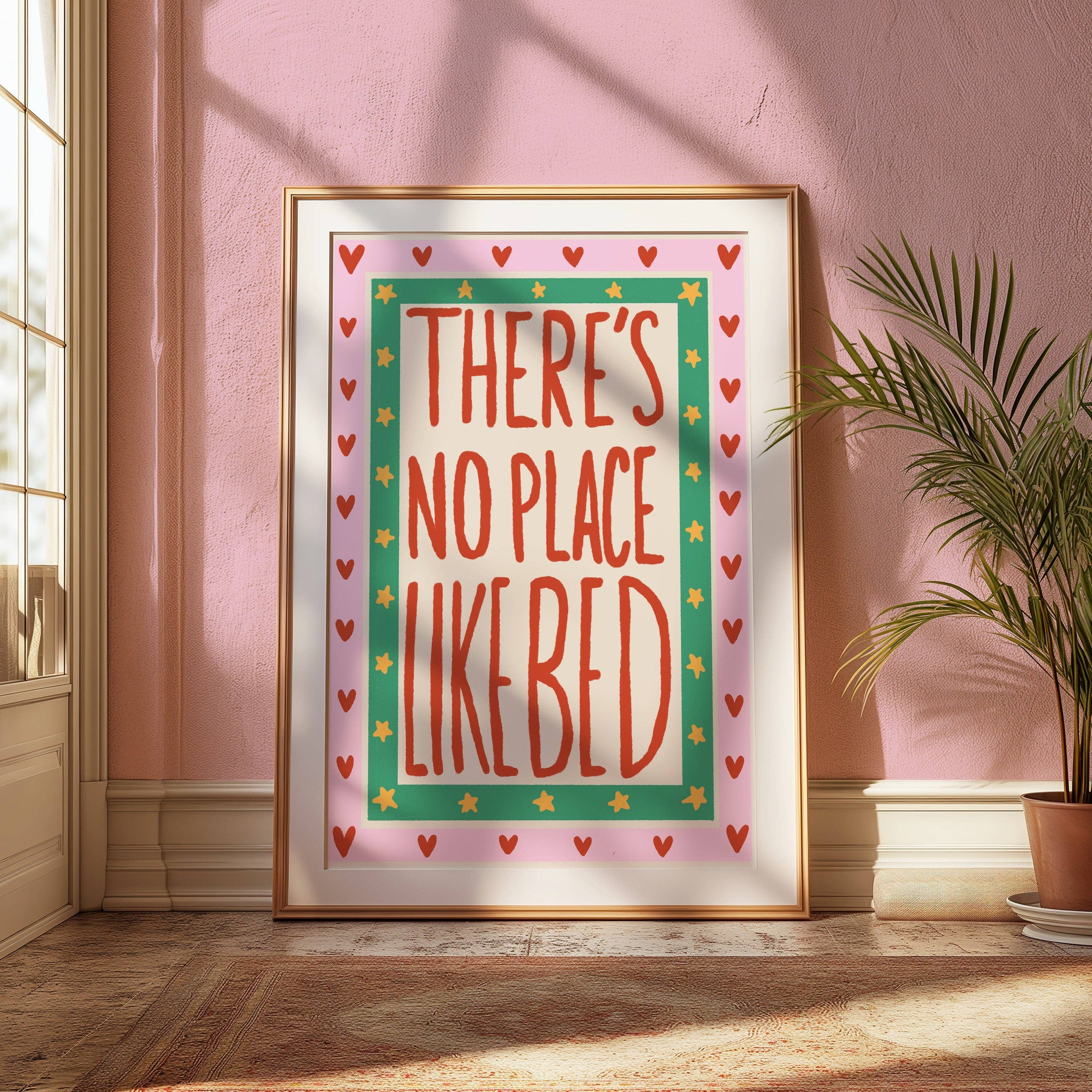 Framed artwork with 'There's no place like bed' text on a pink wall.